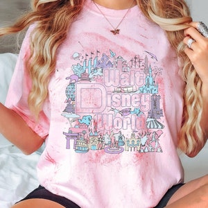 May include: Pink tie-dye t-shirt with a pastel graphic of Walt Disney World landmarks and the park's logo. The design includes illustrations of the castle, Spaceship Earth, and other attractions. The text "Walt Disney World" is prominently displayed.