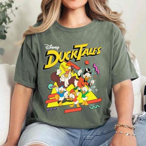 May include: A green t-shirt with a graphic print of the Disney DuckTales characters. The text "Disney DuckTales" is printed in yellow and black.