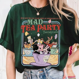 Puede incluir: Camiseta verde oscuro con un gr&aacute;fico colorido de una escena de Mad Tea Party. El dise&ntilde;o incluye personajes en tazas de t&eacute;, con el texto "MAD TEA PARTY FANTASYLAND" en rojo y verde.