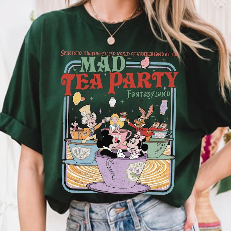 Puede incluir: Camiseta verde oscuro con un gr&aacute;fico colorido de una escena de Mad Tea Party. El dise&ntilde;o incluye personajes en tazas de t&eacute;, con el texto "MAD TEA PARTY FANTASYLAND" en rojo y verde.