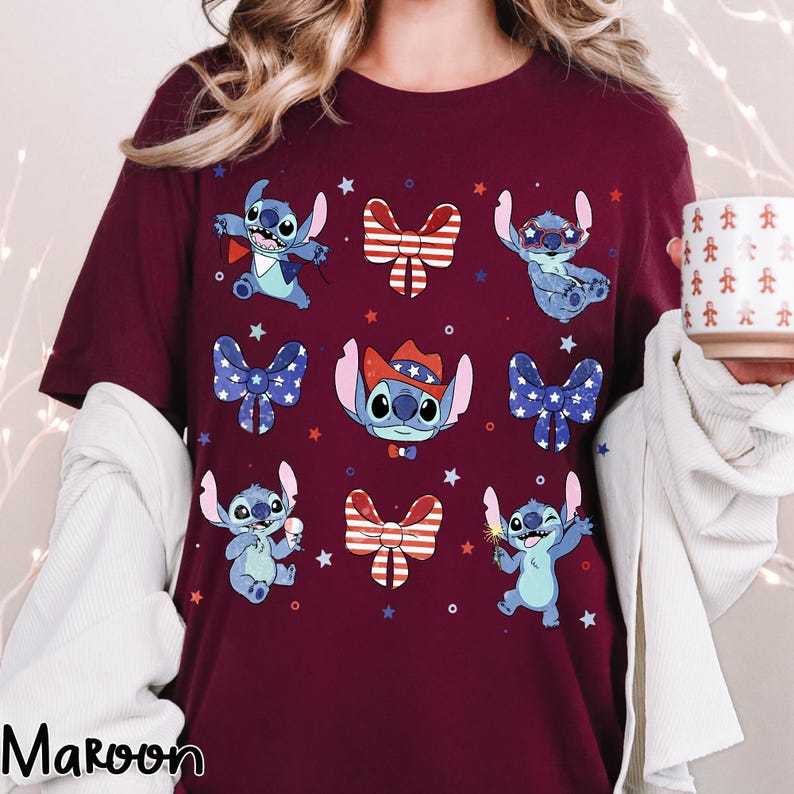 May include: A maroon t-shirt with a pattern of Stitch characters in patriotic poses, surrounded by bow ties and stars. The shirt has a crew neck and short sleeves. The word "Maroon" is printed at the bottom left.