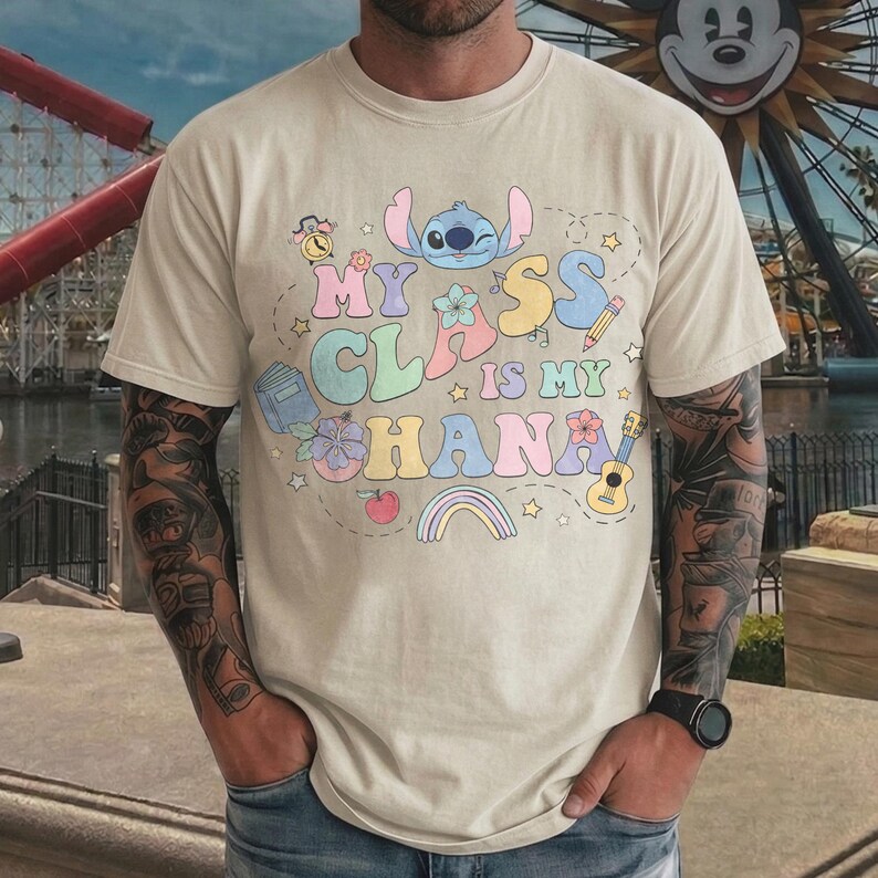 Puede incluir: Camiseta beige con la frase "My Class is My Ohana" en letras coloridas y divertidas. El dise&ntilde;o incluye un personaje de dibujos animados, flores, un arco&iacute;ris y otros elementos caprichosos. La camiseta es de manga corta.