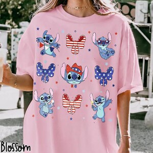 May include: Pink t-shirt with a pattern of the character Stitch in various poses with patriotic bows and stars. The word "Blossom" is printed at the bottom left corner of the shirt.