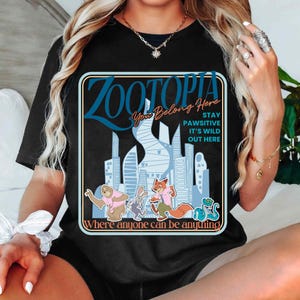 Puede incluir: Camiseta negra con un gr&aacute;fico de Zootopia. El dise&ntilde;o incluye el texto "Zootopia", "You Belong Here" y "Where anyone can be anything". El gr&aacute;fico tambi&eacute;n muestra animales de dibujos animados y edificios de la ciudad en tonos azules y blancos.