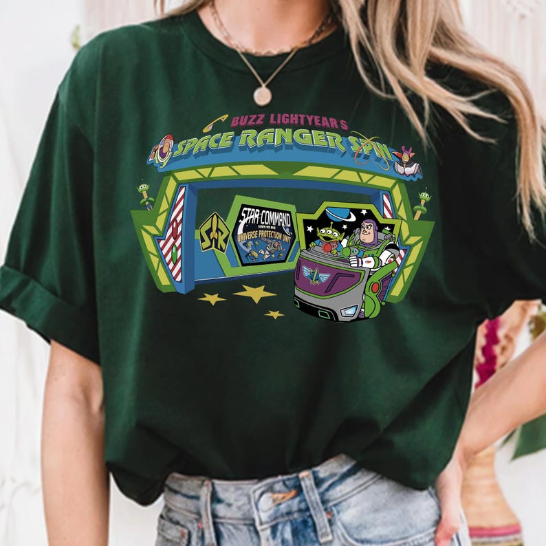K&ouml;nnte beinhalten: Dunkelgr&uuml;nes T-Shirt mit einer farbenfrohen Grafik von Buzz Lightyear's Space Ranger Spin. Das Design zeigt Buzz Lightyear in einem Fahrzeug mit dem Text "Space Ranger Spin" und "Star Command Universe Protection Unit."
