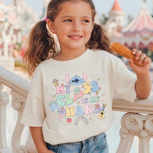 Puede incluir: Una camiseta color crema con el texto "MY CLASS IS MY OHANA" en colores pastel, con un personaje de dibujos animados y otros gr&aacute;ficos. La camiseta la lleva una ni&ntilde;a peque&ntilde;a que sostiene un churro.