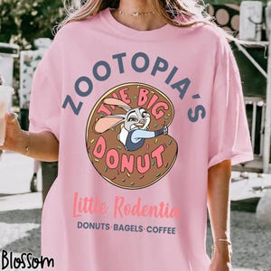 Puede incluir: Camiseta rosa claro con el texto "Zootopia's The Big Donut" y una ilustraci&oacute;n de Judy Hopps dentro de una rosquilla. Debajo, el texto "Little Rodentia" y "DONUTS BAGELS COFFEE".