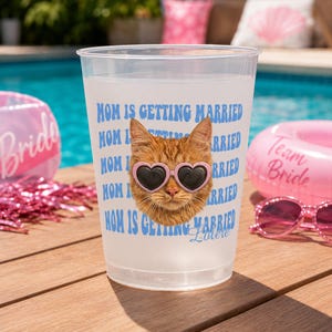May include: A translucent plastic cup featuring a repeating blue text pattern that reads MOM IS GETTING MARRIED. Centered on the cup is a graphic of an orange tabby cat wearing pink heart-shaped sunglasses, with the name Lolere printed below.