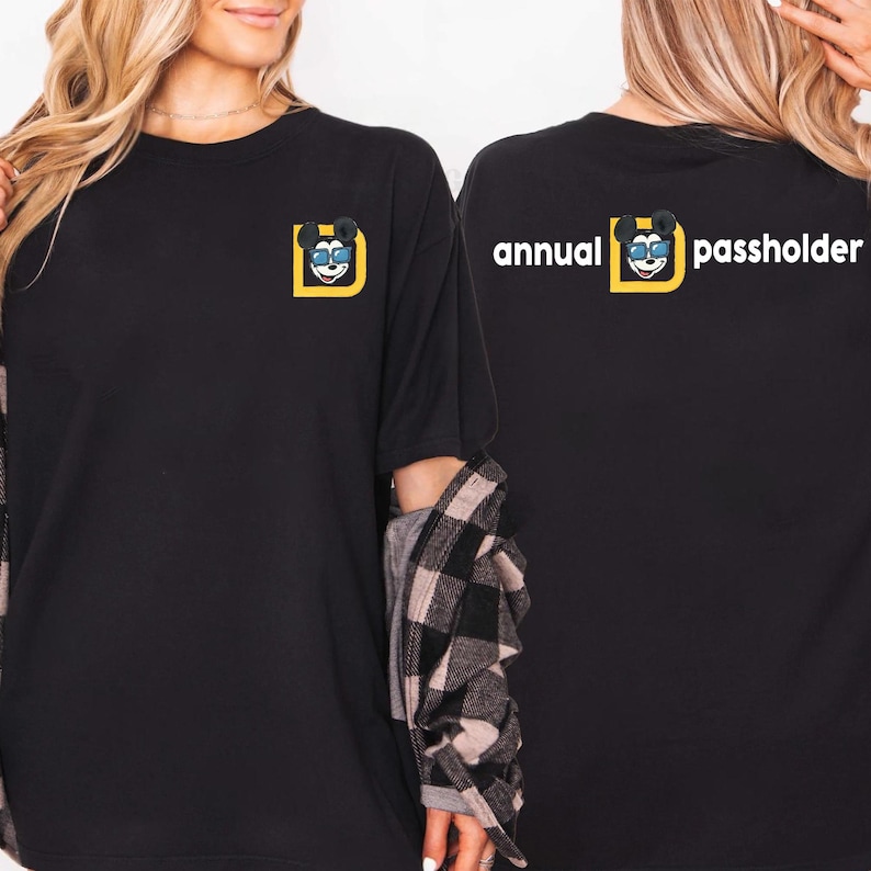 Puede incluir: Camiseta negra con un personaje de dibujos animados con gafas de sol dentro de un cuadrado amarillo. El texto "annual passholder" est&aacute; impreso en la espalda. Estilo casual.
