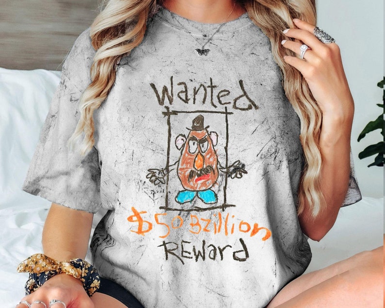 K&ouml;nnte beinhalten: Ein wei&szlig;es T-Shirt mit Used-Look, das eine Comic-Zeichnung von Mr. Potato Head mit dem Text "Wanted 50.000.000.000 $ Reward" zeigt.