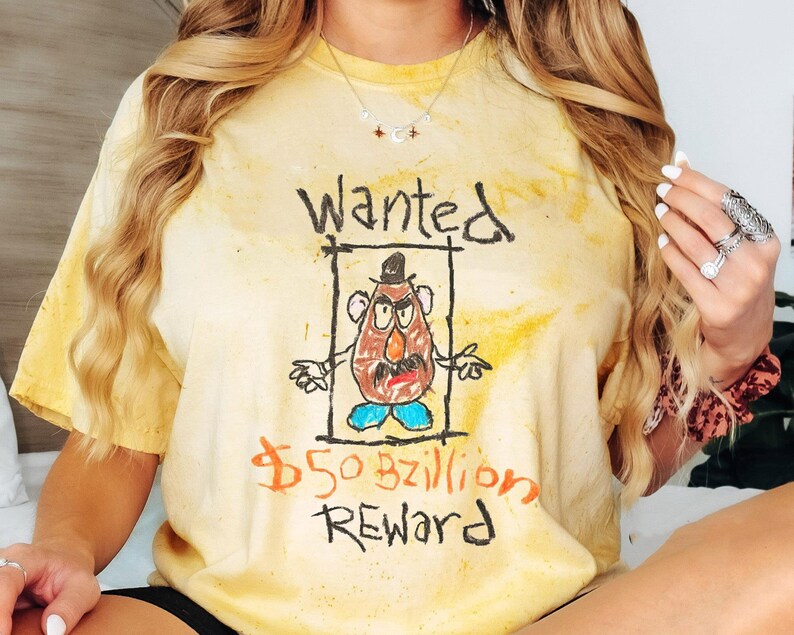 K&ouml;nnte beinhalten: Ein gelbes Batik-T-Shirt mit einem handgezeichneten Fahndungsplakat, auf dem ein Cartoon-Mr. Potato Head abgebildet ist. Das Plakat lautet "Wanted" und "$50 bzillion Reward".