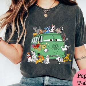 May include: A dark gray t-shirt with a green Volkswagen van with a variety of cartoon dogs and a character from the movie Cars on top. The text "Mon Coeur" is visible on the right sleeve.