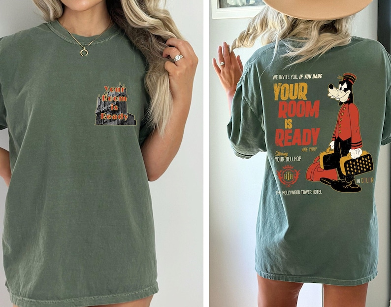 May include: An olive green t-shirt with a graphic on the front that says "Your Room is Ready". The back of the shirt features a cartoon bellhop and the text "We invite you if you dare, Your Room is Ready, Are you Your Bellhop".