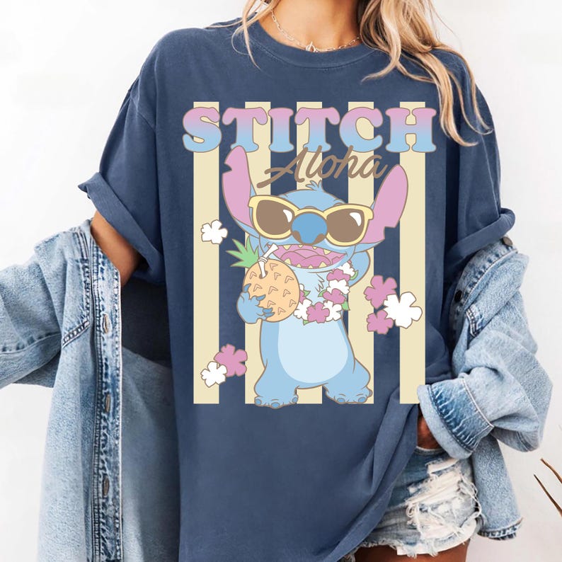 K&ouml;nnte beinhalten: Marineblaues T-Shirt mit einer Zeichentrickfigur, die eine Sonnenbrille tr&auml;gt und eine Ananas h&auml;lt. Das Shirt hat die Worte "STITCH Aloha" in einer bunten Retro-Schriftart mit vertikalen Streifen im Hintergrund.