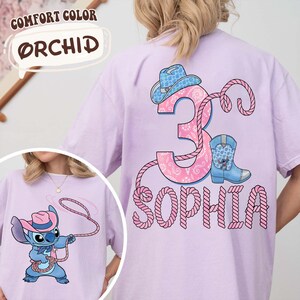 May include: Orchid-colored t-shirt featuring a cartoon character with a cowboy hat and rope. The back of the shirt has a pink number 3, a cowboy hat, a boot, and the name "Sophia" in a rope-like font. The text "COMFORT COLOR" and "ORCHID" are also visible.