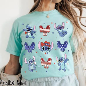 May include: A pale turquoise t-shirt with cartoon Stitch illustrations and patriotic bow tie designs. The shirt includes the text "Chalky Mint" at the bottom. The Stitch characters are surrounded by star shapes.