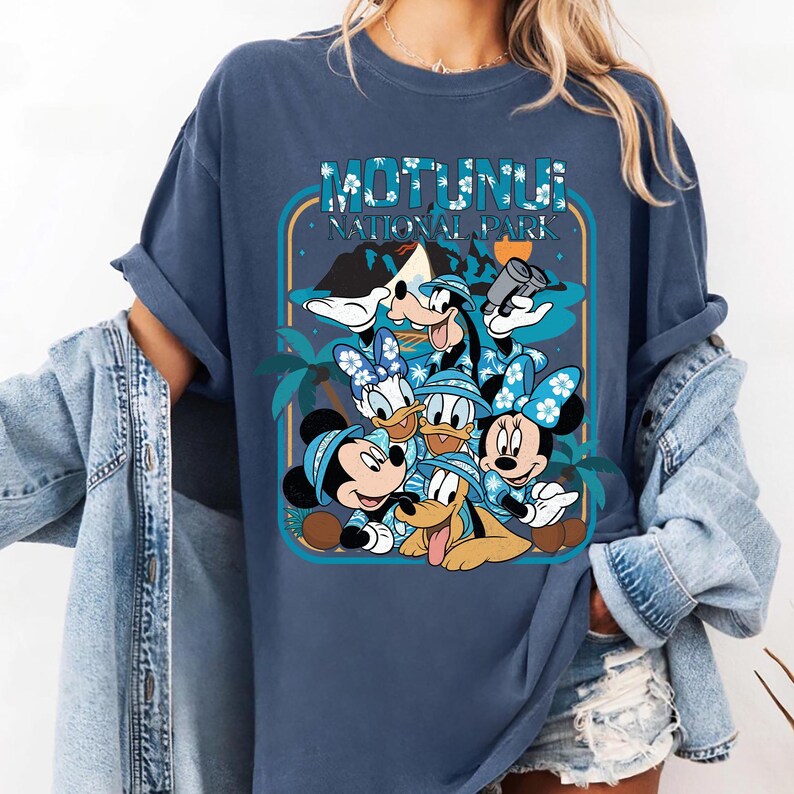 May include: Blue t-shirt featuring a graphic of Disney characters, including Mickey, Minnie, Donald, Daisy, and Goofy, in tropical attire. The design includes the text "MOTUNUI NATIONAL PARK" in a stylized font, set against a tropical backdrop.
