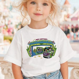 K&ouml;nnte beinhalten: Wei&szlig;es T-Shirt mit einer farbenfrohen Grafik von Buzz Lightyear's Space Ranger Spin. Das Design zeigt das Logo der Attraktion, ein Fahrzeug mit Figuren und die Worte "Star Command".