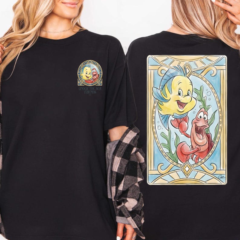 May include: Black t-shirt featuring a colorful illustration of Flounder and Sebastian from The Little Mermaid. The front of the shirt has a small circular graphic with Ariel, Flounder, and Sebastian. Text on the front and back of the shirt reads "Under the Sea Friends".