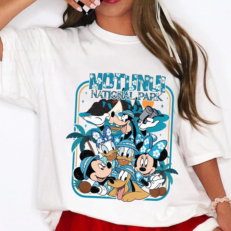 May include: White t-shirt featuring a graphic of Disney characters, including Mickey and Minnie Mouse, Donald and Daisy Duck, Goofy, and Pluto. The graphic is framed by a teal border with the words "Motunui National Park".