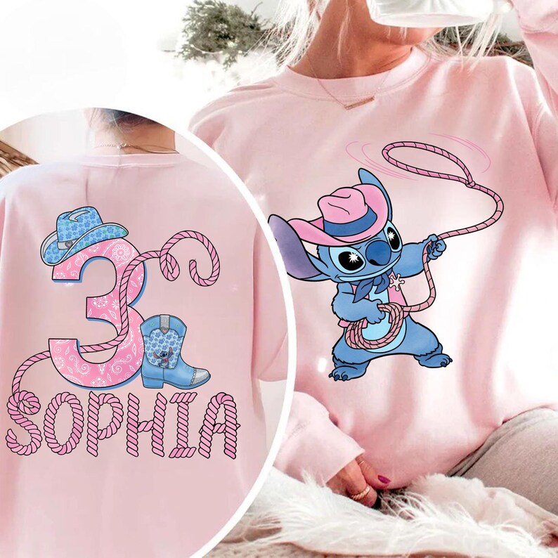 May include: Pink sweatshirt featuring a cartoon character in a cowboy hat holding a lasso. The back of the sweatshirt has a pink design with the number 3, a cowboy hat, a boot, and the name "Sophia".