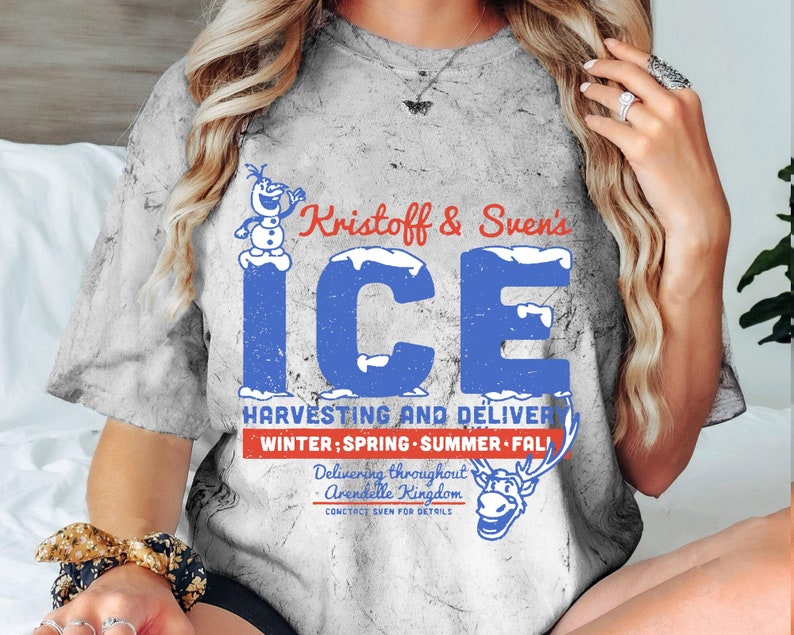 May include: A gray t-shirt with a distressed look featuring a cartoon snowman and reindeer. The text on the shirt reads "Kristoff & Sven's ICE HARVESTING AND DELIVERY WINTER; SPRING - SUMMER - FALL Delivering throughout Arendelle Kingdom CONTACT SVEN FOR DETAILS".