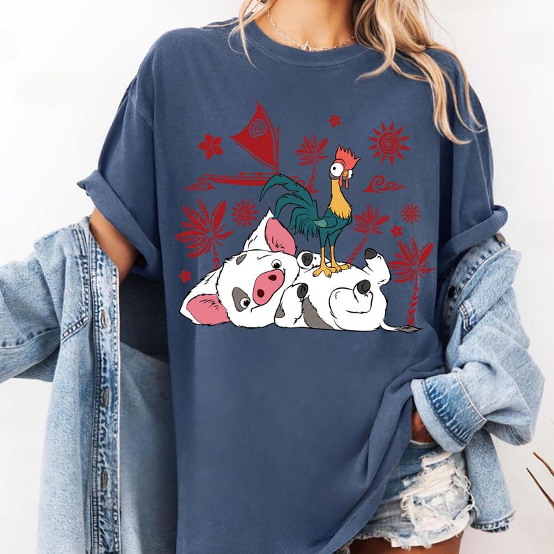 May include: A navy blue t-shirt featuring a graphic of a white pig with pink ears and snout, a green and yellow rooster, and a white pig lying on its back. Red tropical flowers and suns are also printed on the shirt.