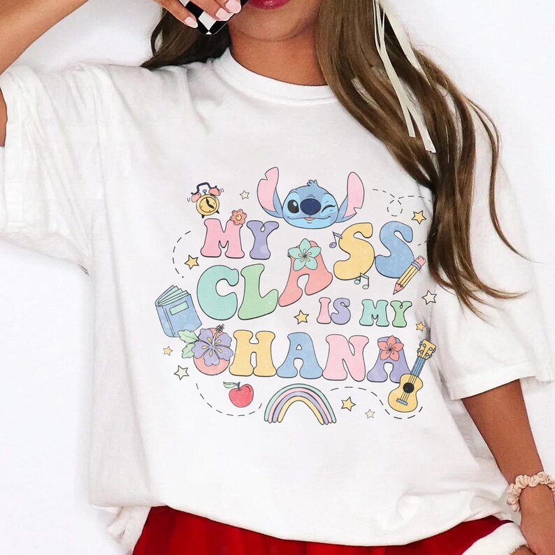 Puede incluir: Camiseta blanca con un gr&aacute;fico colorido que dice "My Class is My Ohana". El dise&ntilde;o incluye un personaje de dibujos animados, estrellas, un arco&iacute;ris e ilustraciones escolares. Una prenda casual para el d&iacute;a a d&iacute;a.