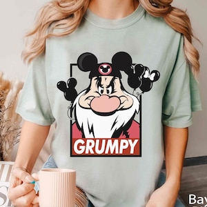 May include: A light green t-shirt with a cartoon image of Grumpy from Snow White and the Seven Dwarfs wearing a red hat with Mickey Mouse ears. The image is in a white box with the word "GRUMPY" in red letters.