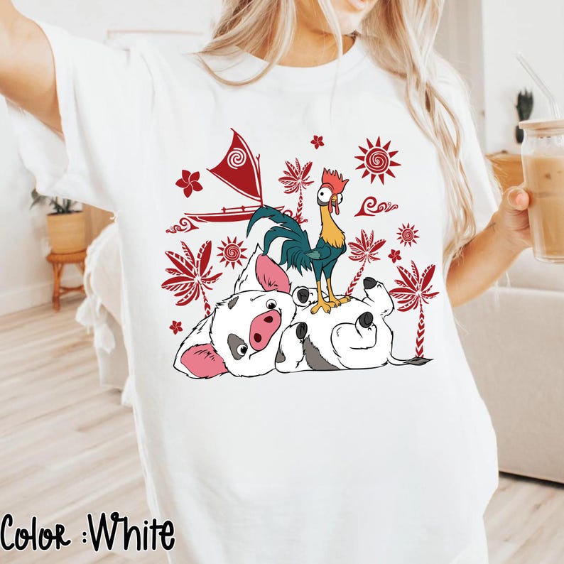 May include: White t-shirt featuring a colorful graphic of a pig, rooster, and boat with red and white accents. The design includes tropical elements like palm trees and suns. The text "Color: White" is at the bottom.