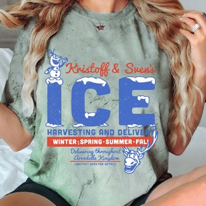May include: A green t-shirt with a distressed look featuring a cartoon snowman and reindeer. The text on the shirt reads "Kristoff & Sven's ICE HARVESTING AND DELIVERY WINTER; SPRING SUMMER FALL Delivering throughout Arendelle Kingdom CONTACT SVEN FOR DETAILS".