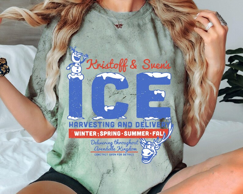 May include: A green t-shirt with a distressed look featuring a cartoon snowman and reindeer. The text on the shirt reads "Kristoff & Sven's ICE HARVESTING AND DELIVERY WINTER; SPRING SUMMER FALL Delivering throughout Arendelle Kingdom CONTACT SVEN FOR DETAILS".