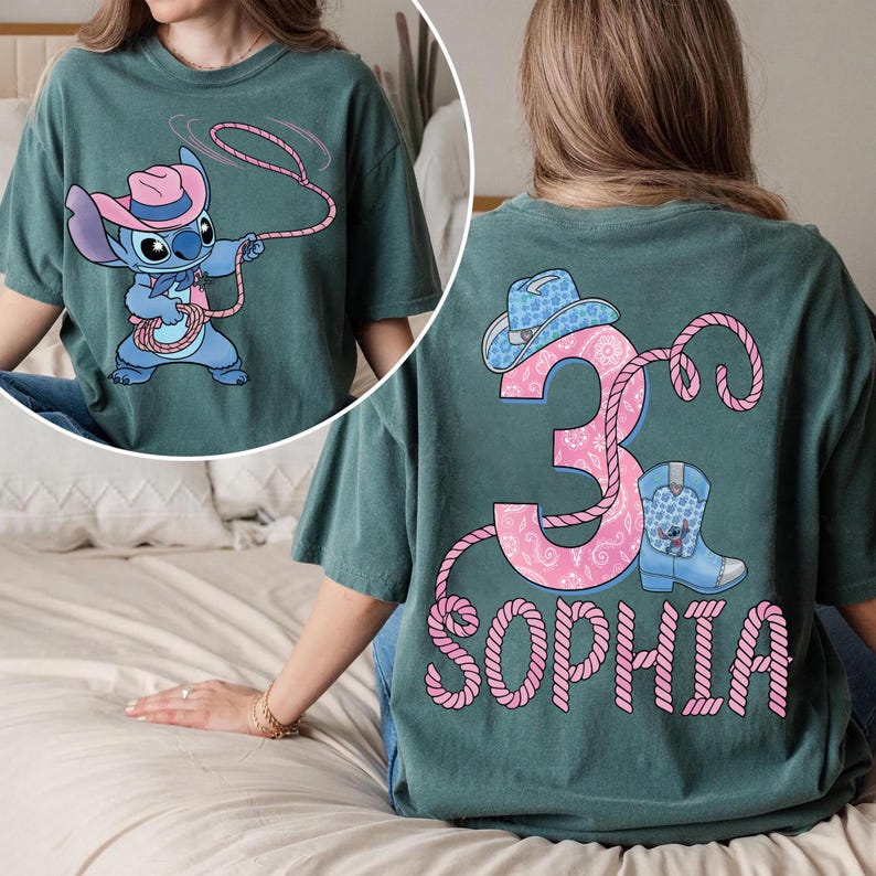May include: Teal green t-shirt featuring a cartoon character in a cowboy hat and lasso. The back of the shirt displays a pink number 3, a cowboy hat, a boot, and the name "SOPHIA" in pink.