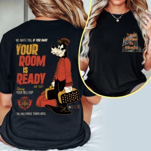 May include: Black t-shirt with a graphic of a bellhop character and the text "YOUR ROOM IS READY" and "THE HOLLYWOOD TOWER HOTEL". The design includes the phrase "WE INVITE YOU, IF YOU DARE". The shirt has a vintage, retro style.