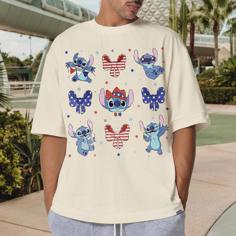 May include: Cream-coloured t-shirt featuring cartoon Stitch characters in various poses with patriotic bow ties and stars. The design includes Stitch wearing a cowboy hat. A fun and festive graphic tee.