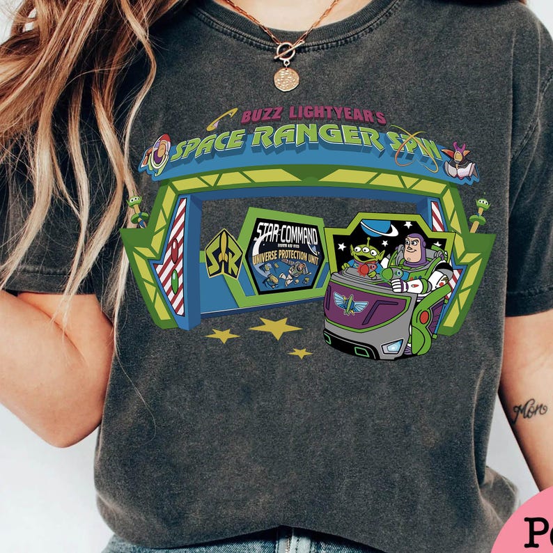 K&ouml;nnte beinhalten: Dunkelgraues T-Shirt mit einer farbenfrohen Grafik von Buzz Lightyear's Space Ranger Spin. Das Design zeigt den Eingang der Attraktion, Buzz Lightyear und die kleinen gr&uuml;nen M&auml;nnchen. Der Text auf dem Shirt lautet "Buzz Lightyear's Space Ranger Spin" und "Star Command".