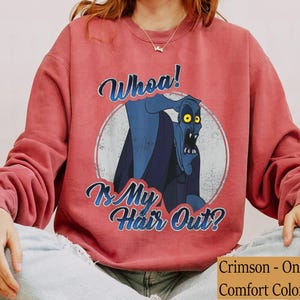 Puede incluir: Sudadera de color carmes&iacute; con un gr&aacute;fico desgastado de un personaje de dibujos animados azul con ojos amarillos. El texto "Whoa! Is My Hair Out?" est&aacute; escrito arriba y abajo del personaje en azul. Es una camiseta Comfort Color.