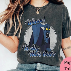 Puede incluir: Camiseta gris oscuro con una imagen de dibujos animados de un personaje azul con ojos amarillos dentro de un c&iacute;rculo blanco. El texto "Whoa! Is My Hair Out?" est&aacute; escrito arriba y debajo del personaje en escritura azul.