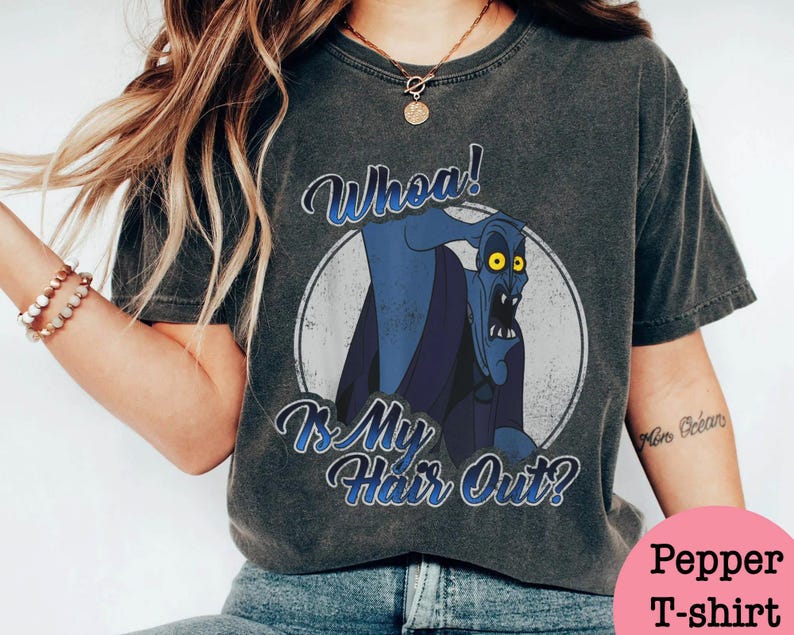 Puede incluir: Camiseta gris oscuro con una imagen de dibujos animados de un personaje azul con ojos amarillos dentro de un c&iacute;rculo blanco. El texto "Whoa! Is My Hair Out?" est&aacute; escrito arriba y debajo del personaje en escritura azul.