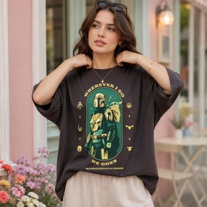 Peut inclure: T-shirt gris fonc&eacute; avec un motif de The Mandalorian et Grogu, et le texte "WHEREVER I GO HE GOES". Le design est dans un ovale vert, avec des accents jaunes et blancs. Coupe ample et d&eacute;contract&eacute;e.