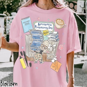 Puede incluir: Camiseta rosa con un gr&aacute;fico que celebra el D&iacute;a de los Profesionales Administrativos 2026. El dise&ntilde;o incluye una oveja de dibujos animados, libros, una taza de caf&eacute; y material de oficina. La camiseta tambi&eacute;n presenta el texto "Assistant Mayor".
