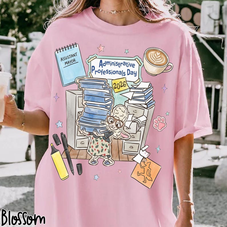 Puede incluir: Camiseta rosa con un gr&aacute;fico que celebra el D&iacute;a de los Profesionales Administrativos 2026. El dise&ntilde;o incluye una oveja de dibujos animados, libros, una taza de caf&eacute; y material de oficina. La camiseta tambi&eacute;n presenta el texto "Assistant Mayor".