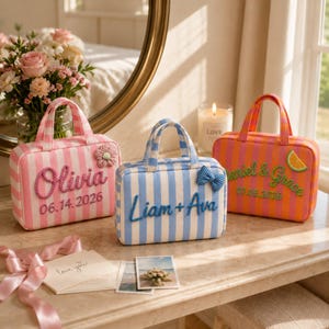 May include: Three rectangular fabric bags with top handles and vertical stripes. The pink bag features the name Olivia and date 06.14.2026. The blue bag displays Liam + Ava. The orange bag shows Daniel & Grace with the date 07.05.2026.