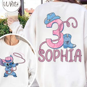 May include: White sweatshirt featuring a cartoon Stitch character with a lasso and a pink cowboy hat. The back of the sweatshirt has a pink number 3, a blue cowboy boot, and the name "SOPHIA" in pink.