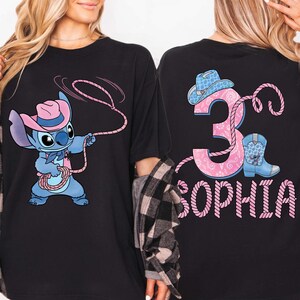 May include: Black t-shirt featuring a cartoon Stitch character in a cowboy hat, roping. The back of the shirt displays the number 3, a cowboy boot, and the name "SOPHIA" in pink.