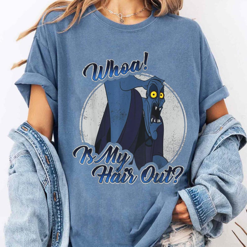 Puede incluir: Camiseta azul con una ilustraci&oacute;n de dibujos animados de un personaje azul con ojos amarillos y el texto "Whoa! Is My Hair Out?" en una fuente estilizada. El personaje est&aacute; sobre un c&iacute;rculo blanco.