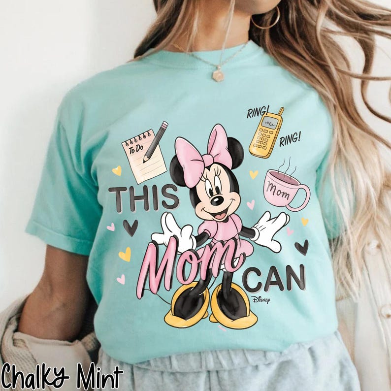 Może przedstawiać: Jasnoniebieska koszulka z grafiką Myszki Minnie w kolorze r&oacute;żowym i czarnym. Tekst "THIS MOM CAN" jest wyświetlany z ilustracjami listy rzeczy do zrobienia, telefonu i filiżanki kawy. Koszulka jest oznaczona jako "Chalky Mint".