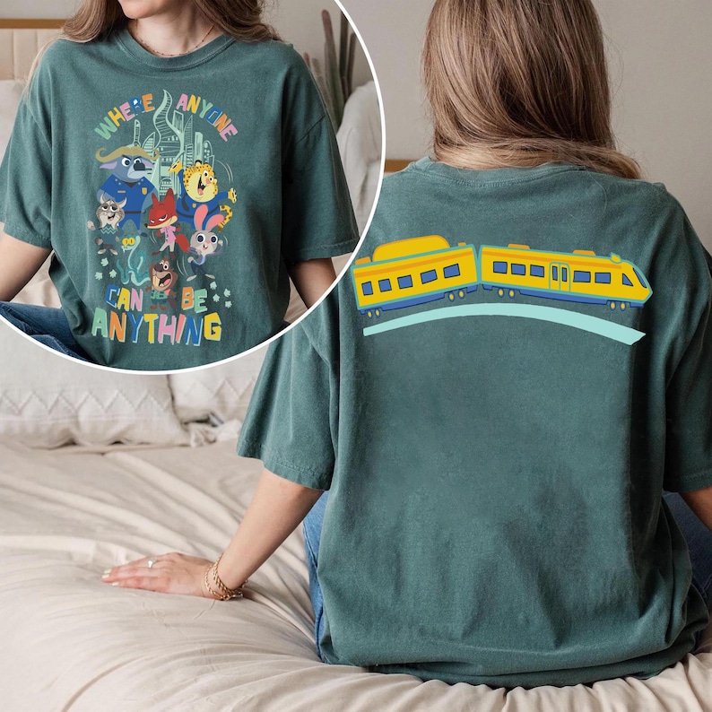 Pu&ograve; includere: T-shirt color verde acqua con una grafica colorata di personaggi dei cartoni animati e la scritta "WHERE ANYONE CAN BE ANYTHING" sul davanti. Il retro della maglietta presenta un disegno di un treno giallo con dettagli blu.