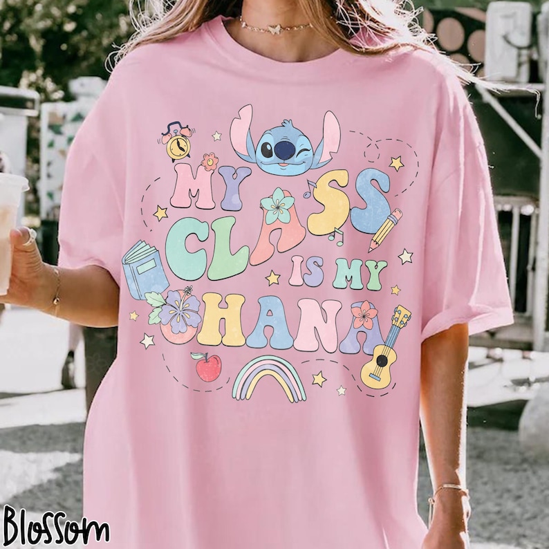 Puede incluir: Camiseta rosa claro con la frase "My Class is My Ohana" en letras de burbujas coloridas, con un personaje de dibujos animados y gr&aacute;ficos escolares. La camiseta tiene mangas cortas y un corte holgado.