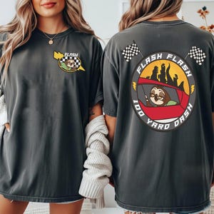 May include: Dark gray t-shirt with a cartoon sloth driving a red car, the text "FLASH FLASH 100 YARD DASH" is printed on the back. The front of the shirt has a smaller version of the sloth and car design with the word "FLASH".